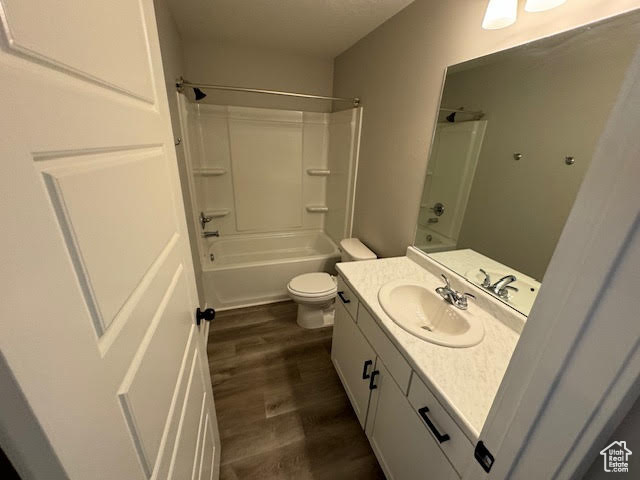 Full bathroom with wood-type flooring, large vanity, toilet, and shower / washtub combination