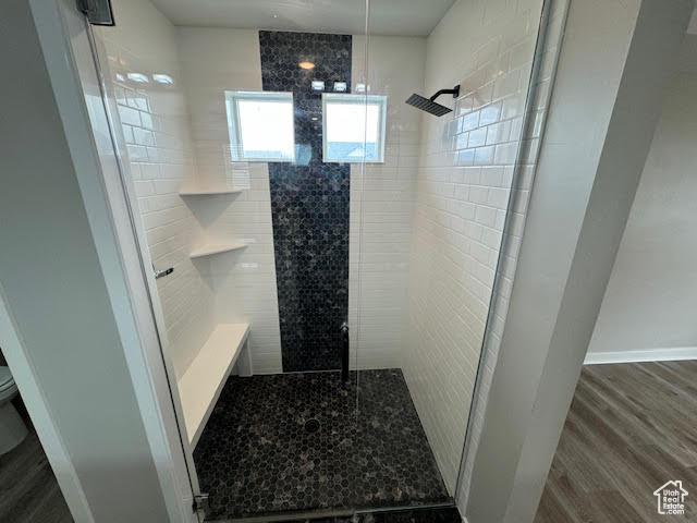 Bathroom with hardwood / wood-style floors, a shower, tile walls, and toilet