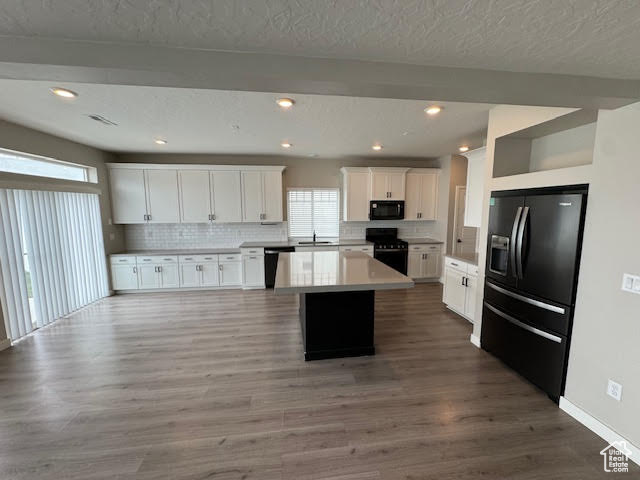 Kitchen featuring white cabinetry, black appliances, hardwood / wood-style floors, and a kitchen island