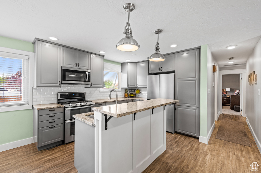 Kitchen featuring a center island, decorative light fixtures, gray cabinets, hardwood / wood-style floors, and appliances with stainless steel finishes