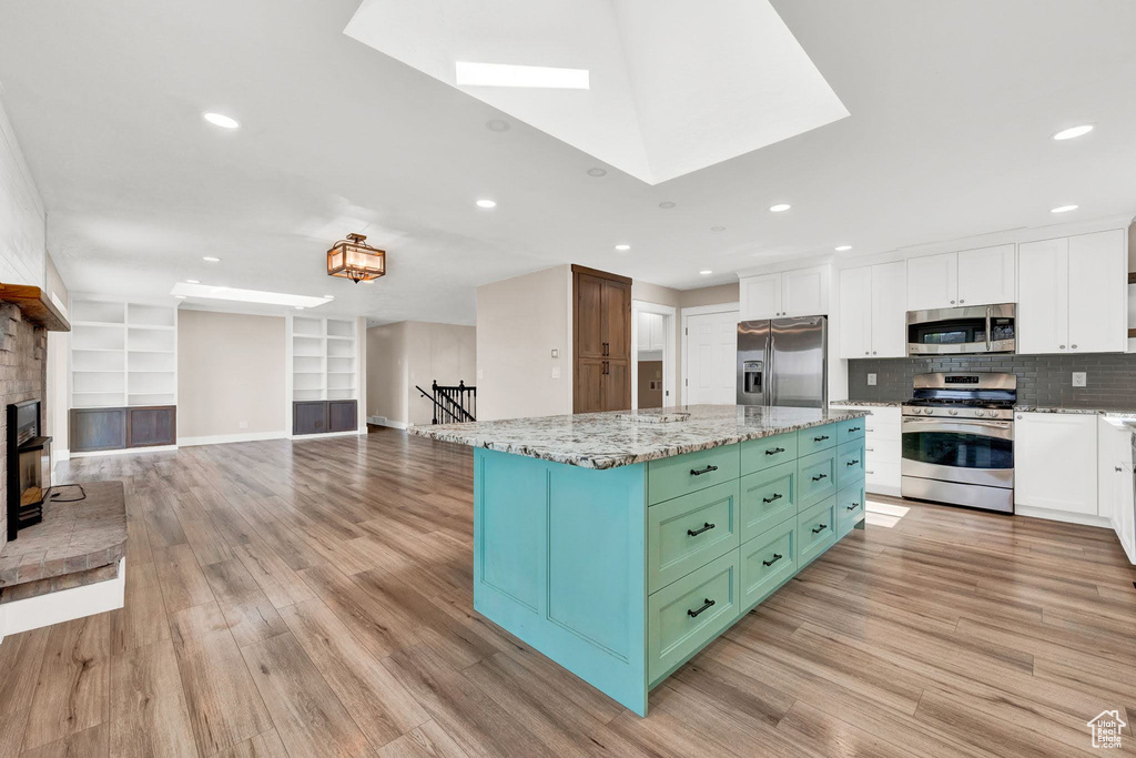 Kitchen with white cabinets, a skylight, light hardwood / wood-style flooring, stainless steel appliances, and a kitchen island