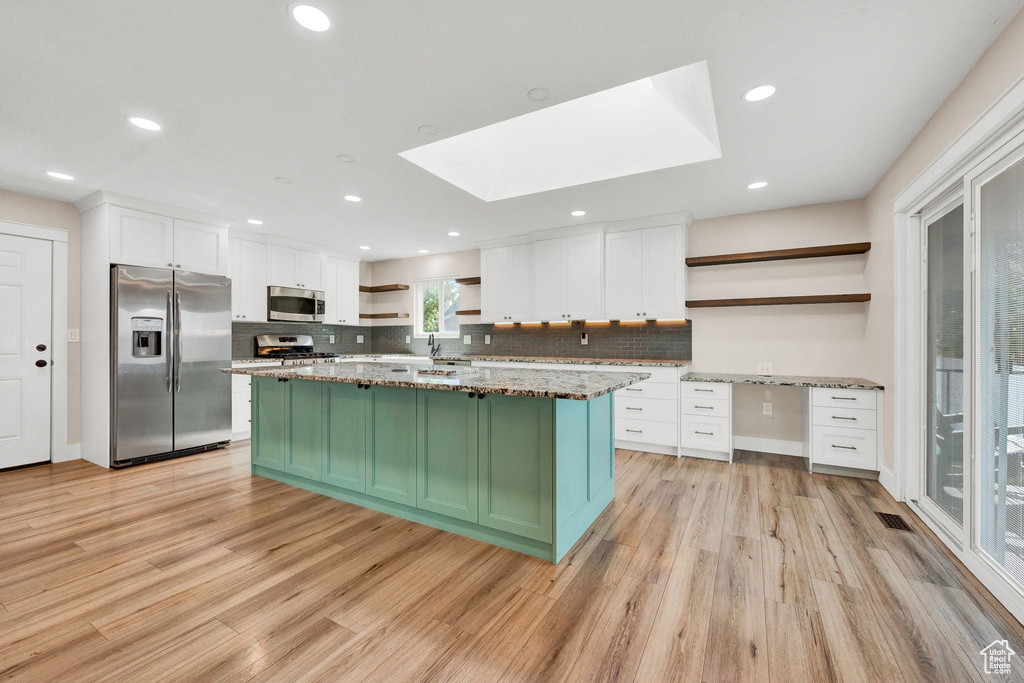 Kitchen with appliances with stainless steel finishes, light hardwood / wood-style floors, a skylight, and white cabinets