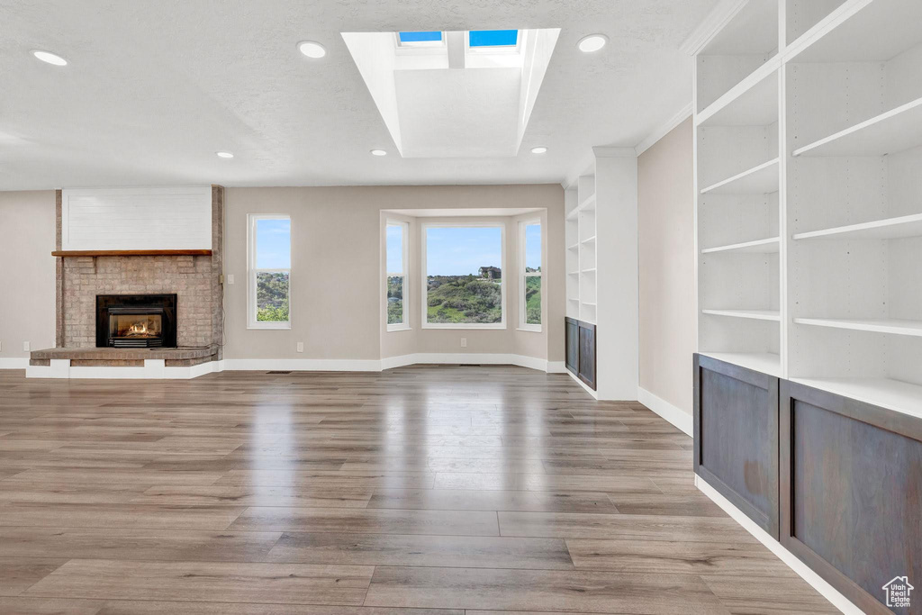 Unfurnished living room featuring a skylight, a fireplace, and light hardwood / wood-style flooring
