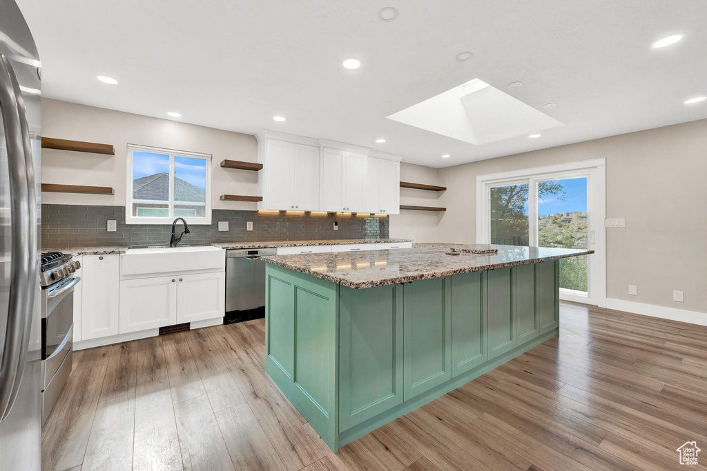 Kitchen with a skylight, appliances with stainless steel finishes, white cabinets, and plenty of natural light