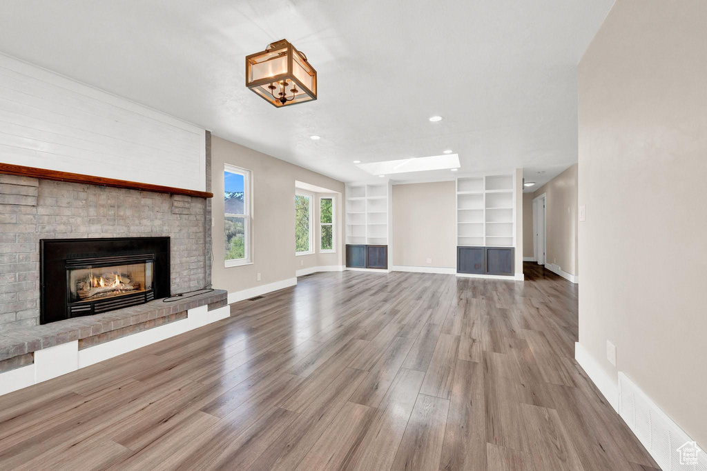 Unfurnished living room with hardwood / wood-style flooring, built in features, and a brick fireplace