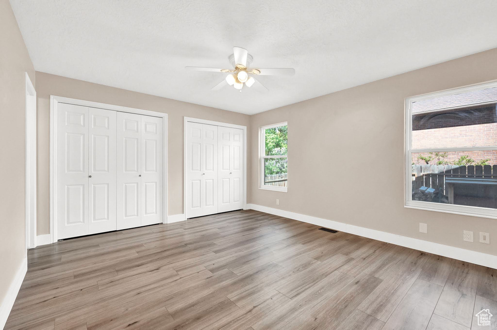 Unfurnished bedroom with multiple closets, ceiling fan, and hardwood / wood-style flooring