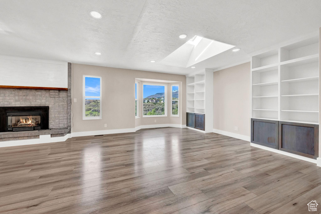 Unfurnished living room with a skylight, wood-type flooring, built in features, and a textured ceiling