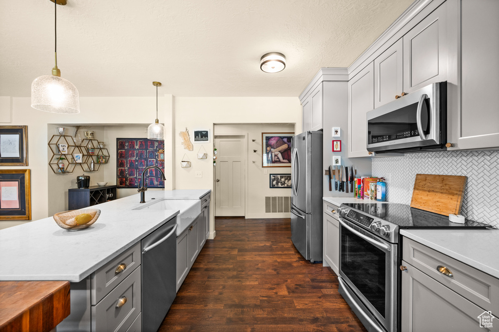Kitchen featuring appliances with stainless steel finishes, sink, backsplash, dark hardwood / wood-style flooring, and hanging light fixtures
