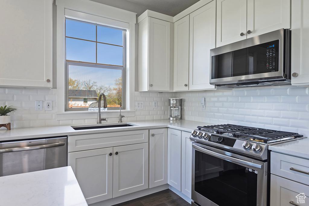 Kitchen featuring sink, stainless steel appliances, tasteful backsplash, white cabinets, and a wealth of natural light