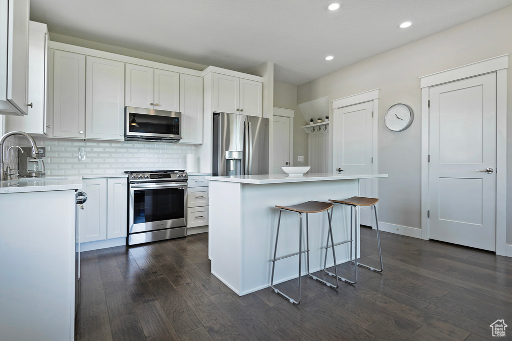 Kitchen with white cabinets, a kitchen island, stainless steel appliances, and dark hardwood / wood-style flooring