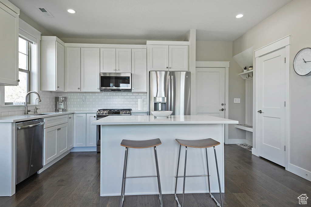 Kitchen featuring appliances with stainless steel finishes, a center island, sink, white cabinetry, and dark hardwood / wood-style flooring