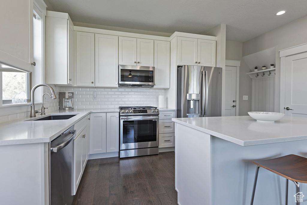 Kitchen featuring backsplash, stainless steel appliances, dark wood-type flooring, white cabinetry, and sink