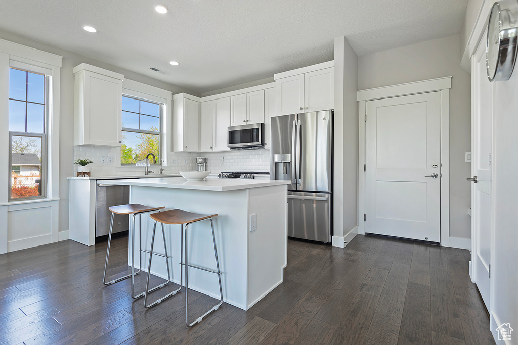 Kitchen featuring appliances with stainless steel finishes, dark wood-type flooring, backsplash, and white cabinetry