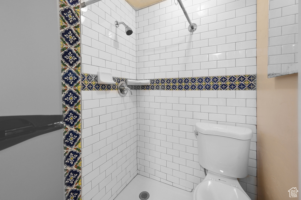 Bathroom with tiled shower, toilet, and tile walls