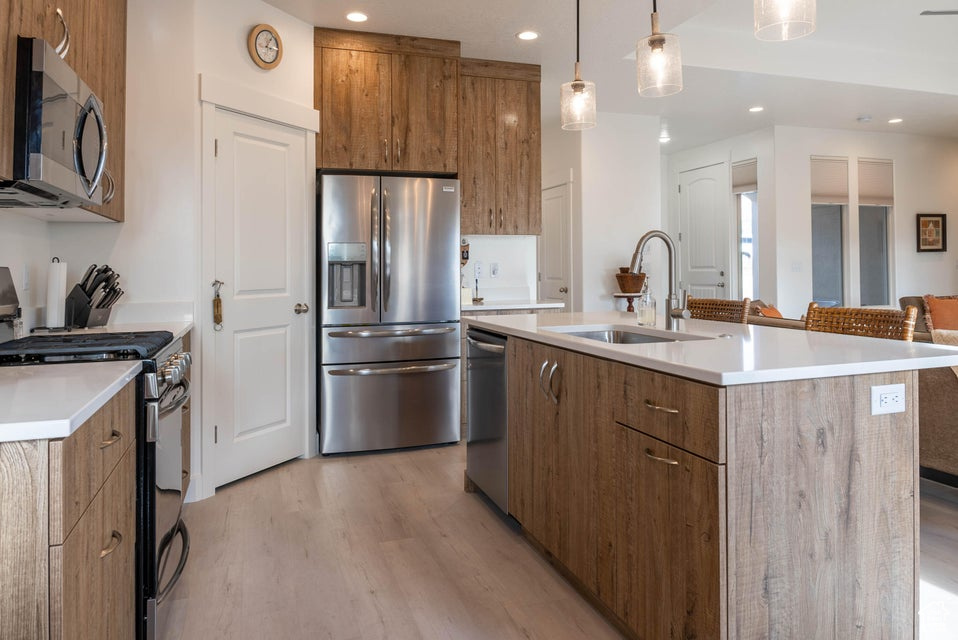 Kitchen featuring appliances with stainless steel finishes, light hardwood / wood-style flooring, hanging light fixtures, a center island with sink, and sink