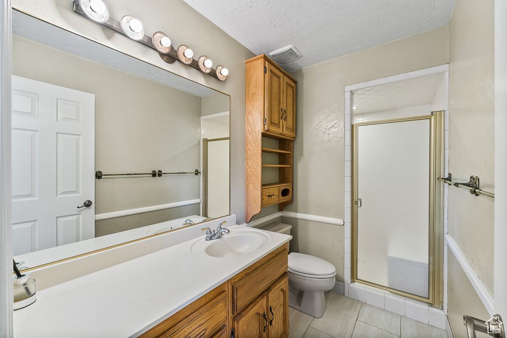 Bathroom with large vanity, a textured ceiling, walk in shower, tile floors, and toilet