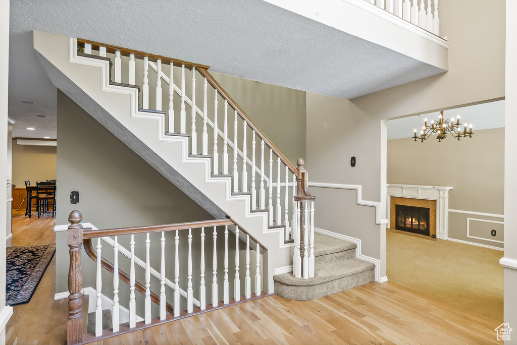 Stairs featuring a chandelier, a premium fireplace, wood-type flooring, and a textured ceiling
