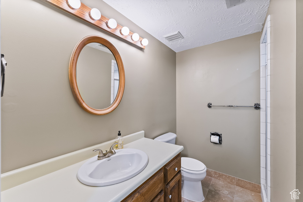 Bathroom featuring tile floors, vanity with extensive cabinet space, toilet, and a textured ceiling