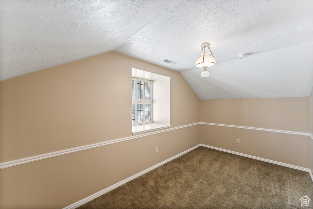 Additional living space featuring a textured ceiling, dark colored carpet, and vaulted ceiling
