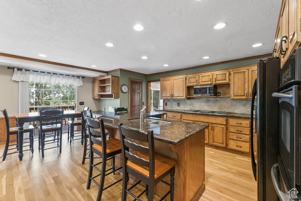 Kitchen featuring appliances with stainless steel finishes, light hardwood / wood-style flooring, a center island with sink, tasteful backsplash, and sink