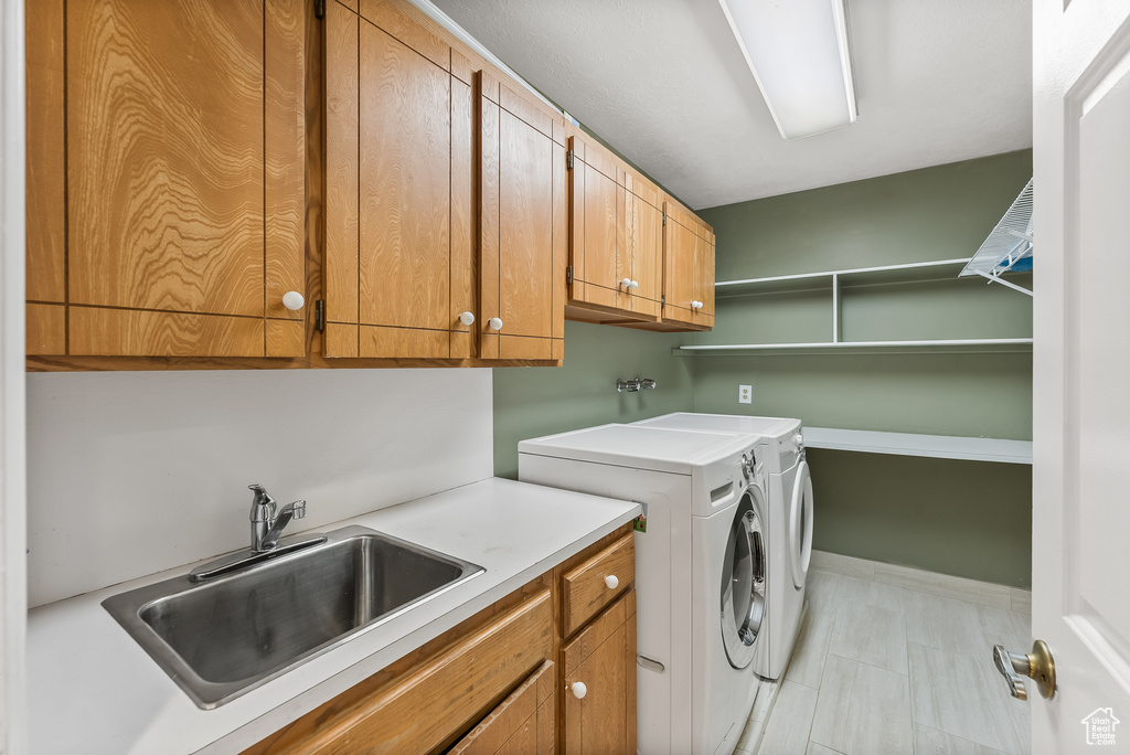 Laundry area with cabinets, sink, light tile flooring, and washing machine and clothes dryer