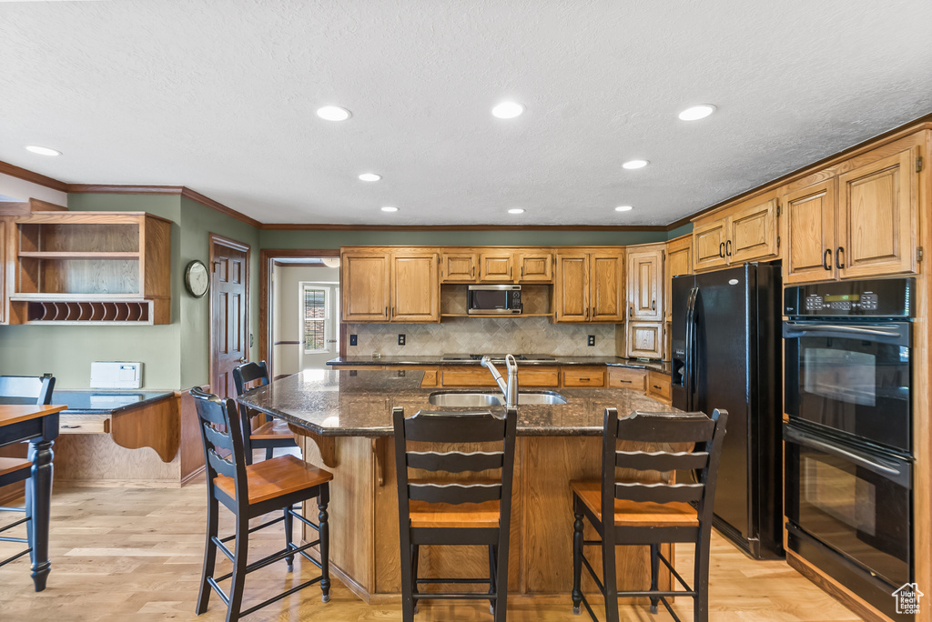 Kitchen with dark stone countertops, light hardwood / wood-style floors, black appliances, and a center island with sink