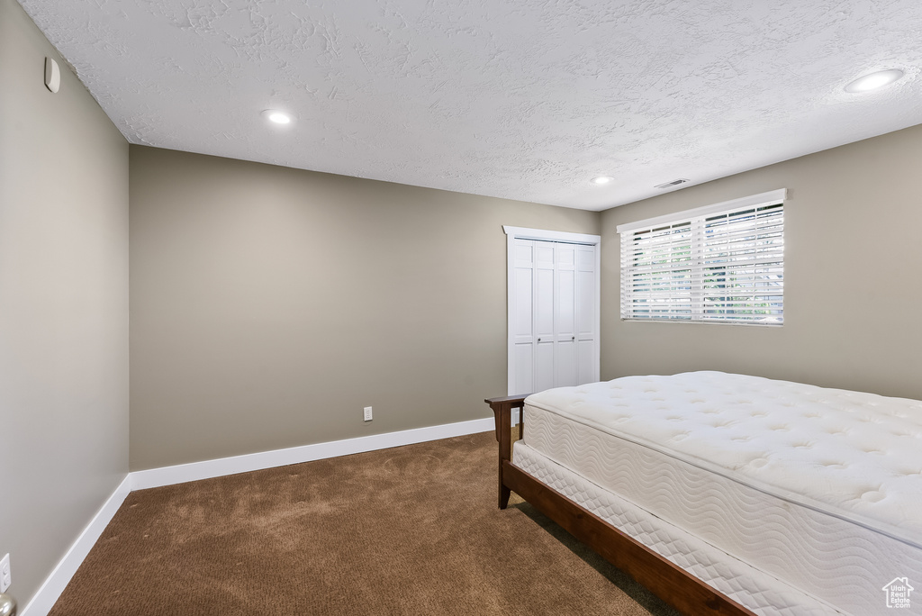 Bedroom featuring a closet, a textured ceiling, and dark carpet