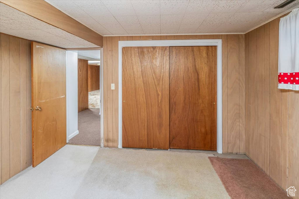 Bedroom with light colored carpet, a closet, and wooden walls