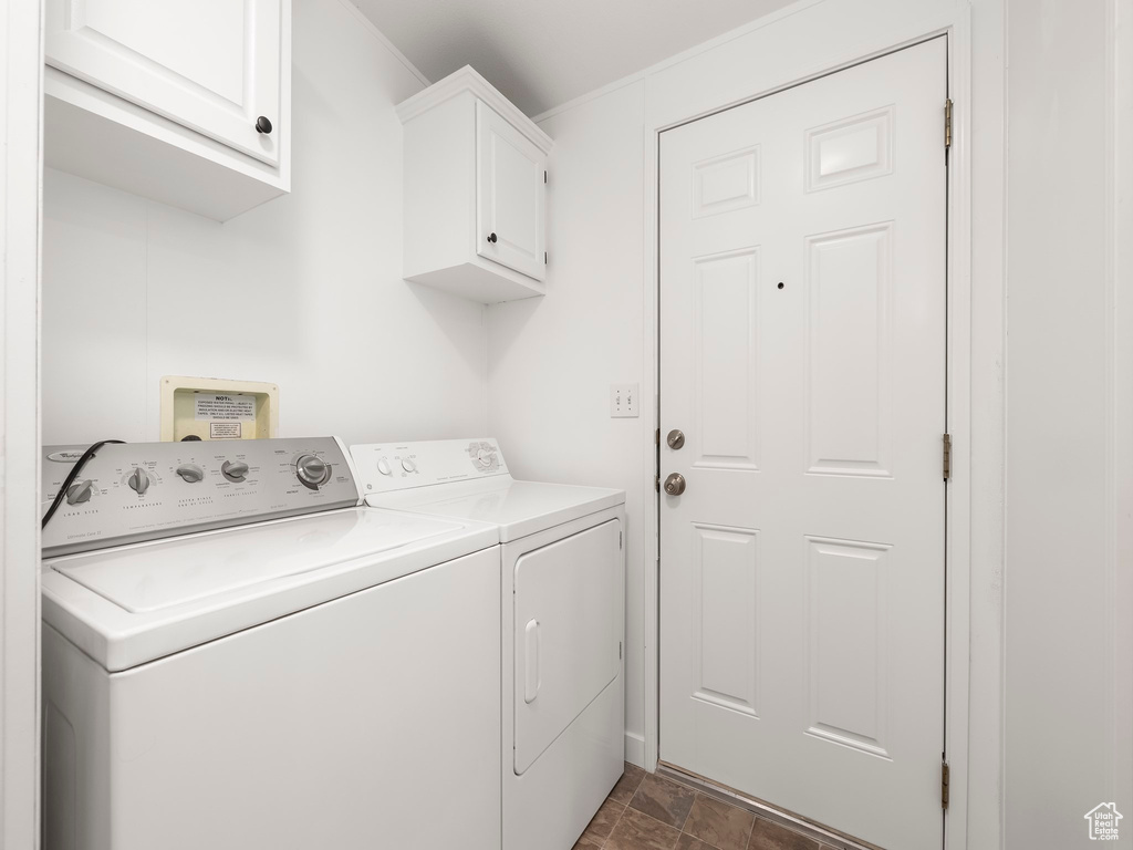 Washroom with washer and clothes dryer, dark tile flooring, and cabinets