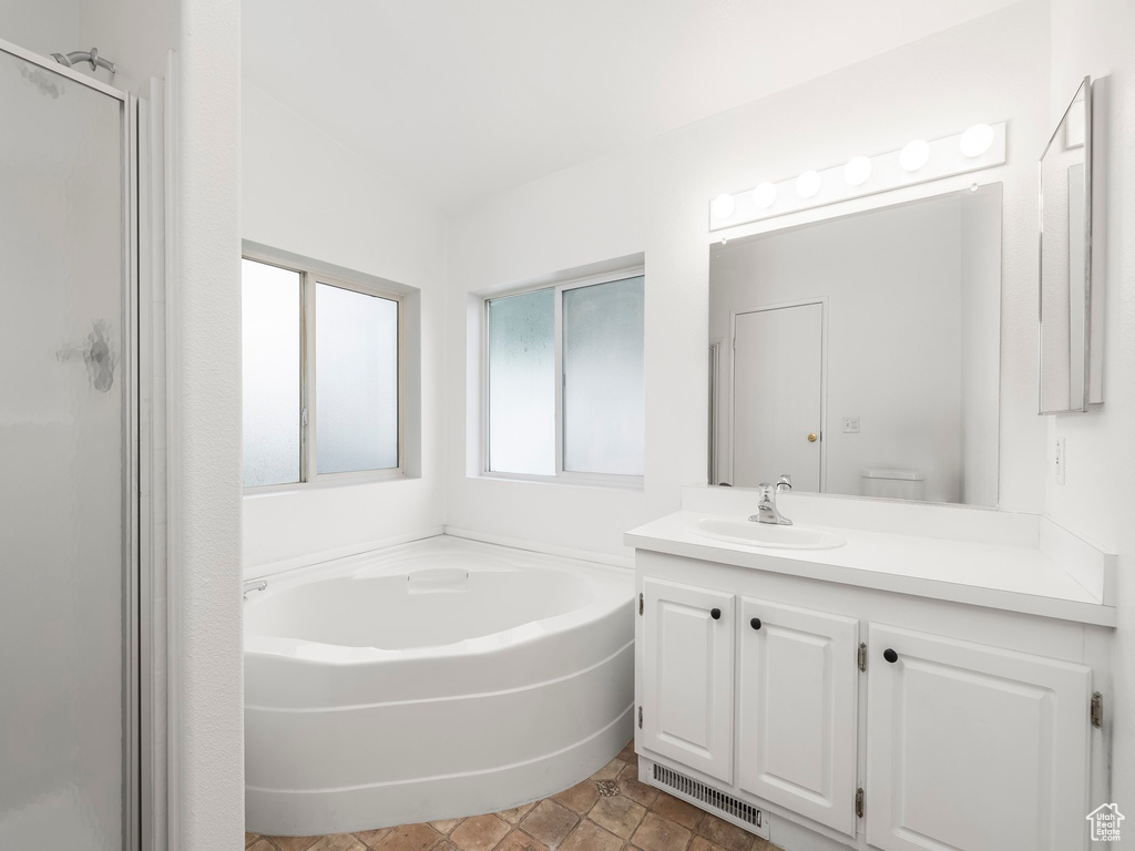 Full bathroom with toilet, independent shower and bath, tile floors, and vanity with extensive cabinet space