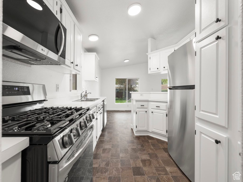 Kitchen with white cabinets, lofted ceiling, and stainless steel appliances