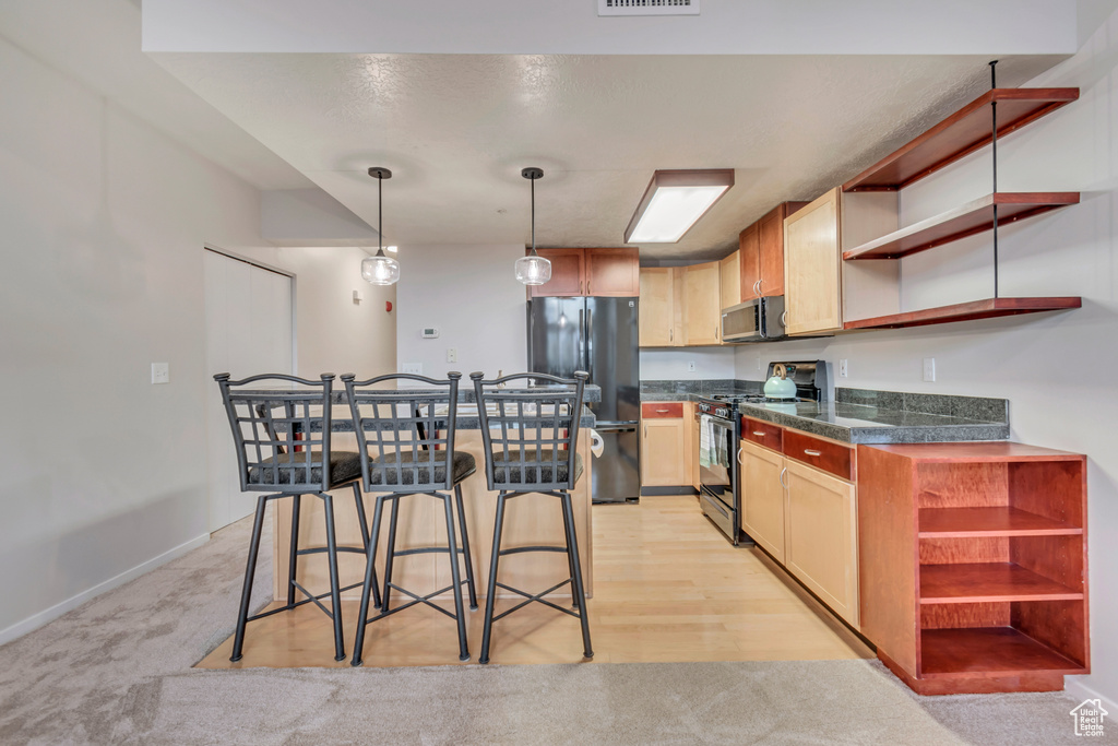 Kitchen with stainless steel appliances, light carpet, a breakfast bar, and decorative light fixtures