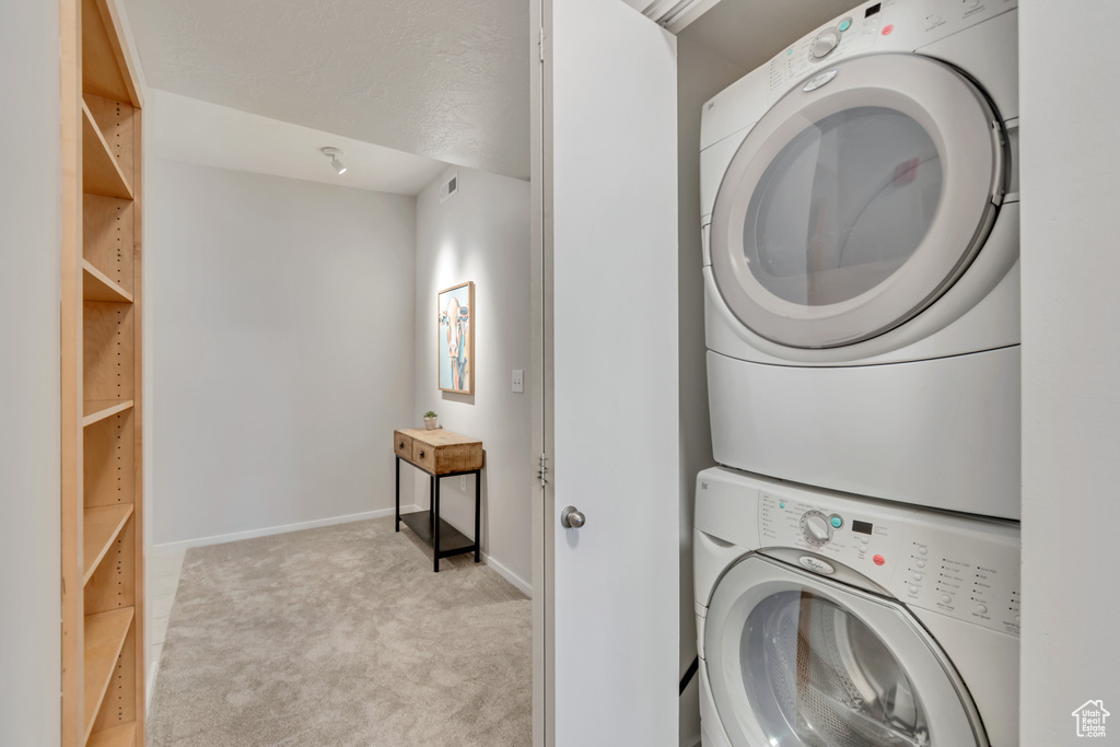 Laundry area featuring light colored carpet and stacked washer / drying machine