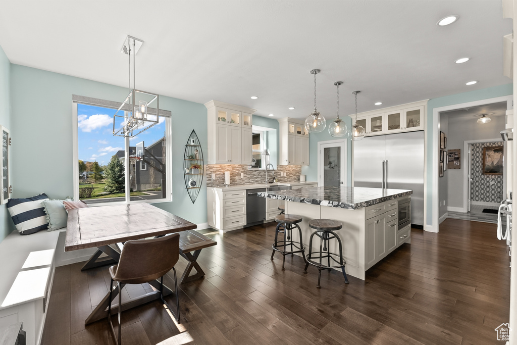 Kitchen featuring a kitchen island, white cabinets, backsplash, decorative light fixtures, and dark hardwood / wood-style floors