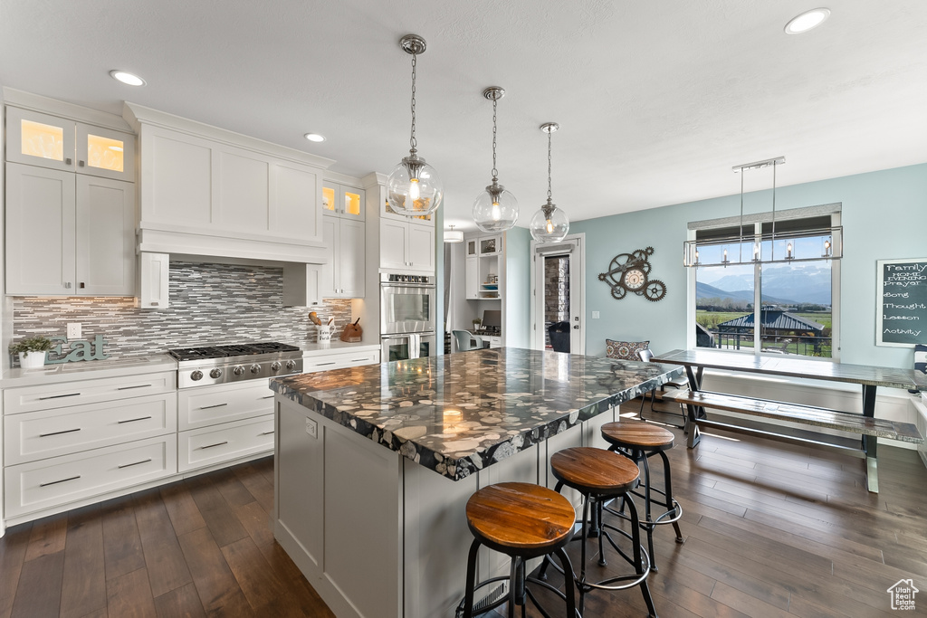 Kitchen with a center island, white cabinets, dark hardwood / wood-style floors, appliances with stainless steel finishes, and tasteful backsplash