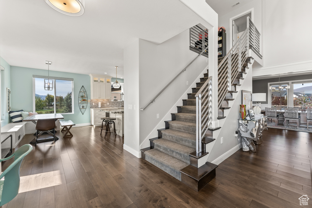 Staircase with an inviting chandelier, a wealth of natural light, and dark hardwood / wood-style floors