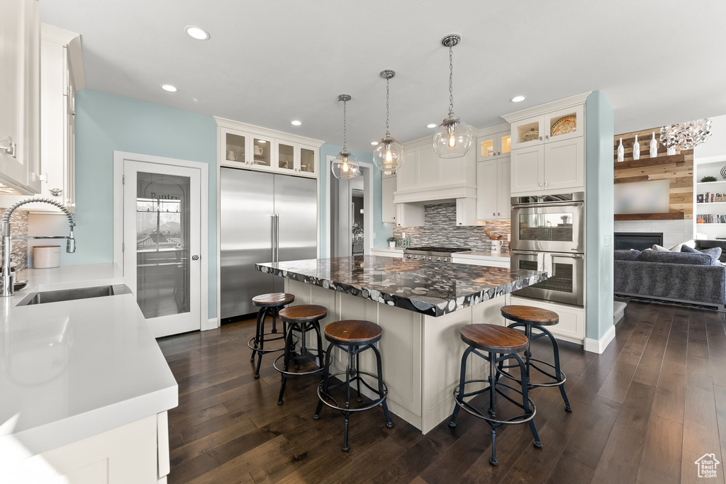 Kitchen featuring dark wood-type flooring, backsplash, stainless steel appliances, sink, and a kitchen island
