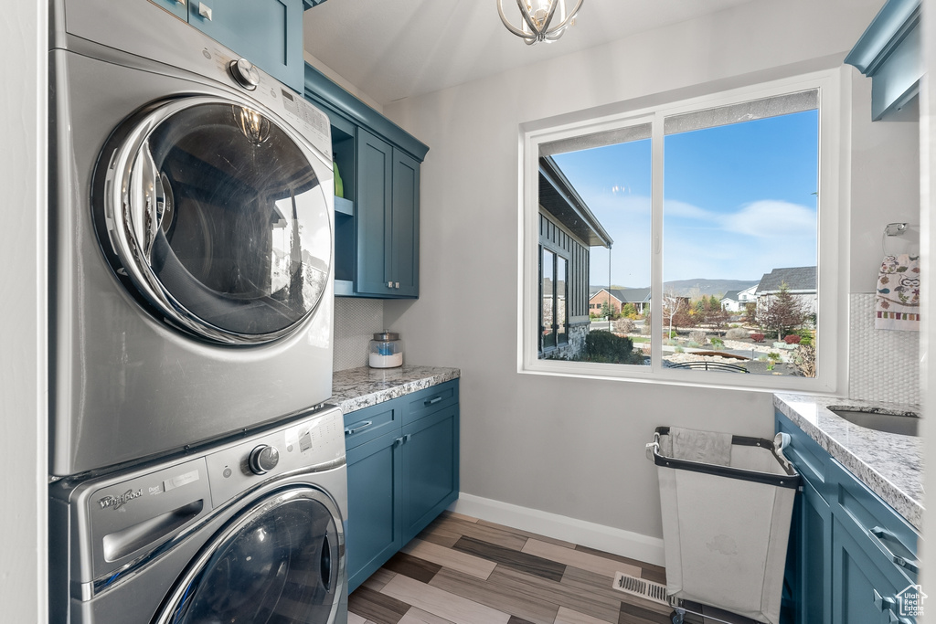 Laundry room with light hardwood / wood-style flooring, cabinets, and stacked washer and clothes dryer