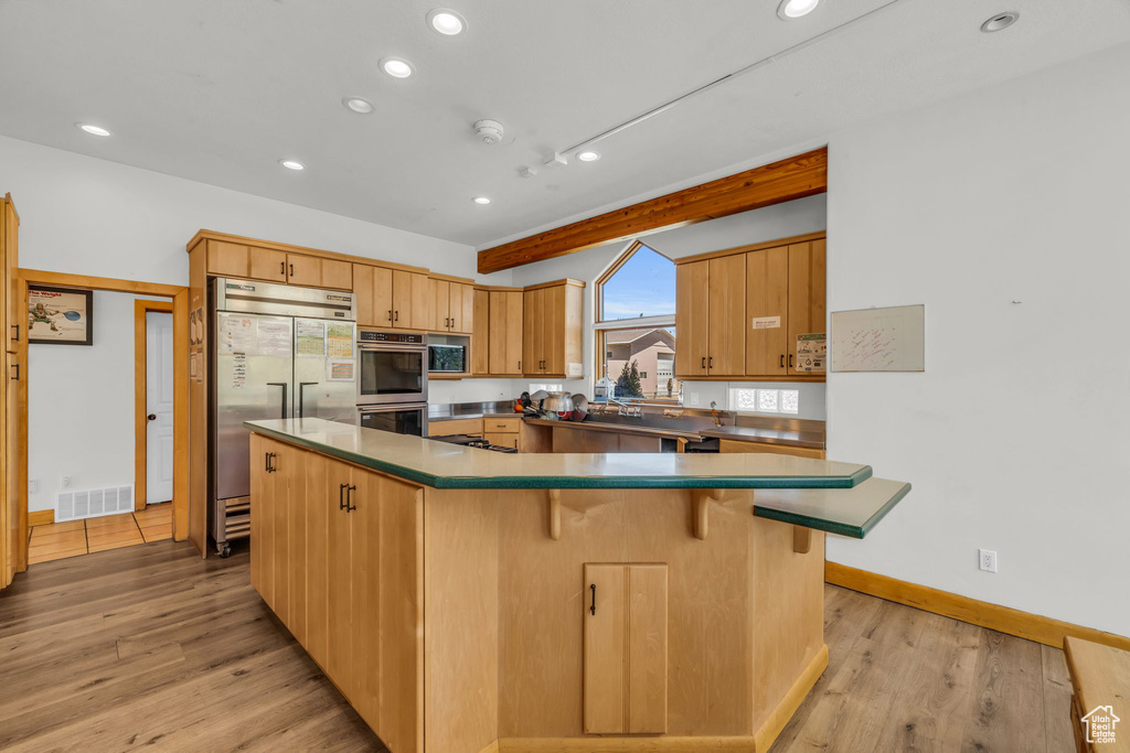 Kitchen with a kitchen breakfast bar, stainless steel appliances, a spacious island, and light wood-type flooring
