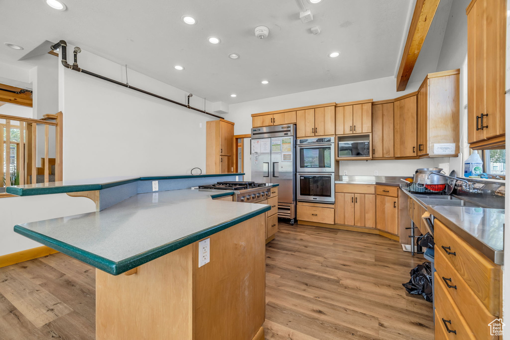 Kitchen featuring built in appliances, light hardwood / wood-style flooring, beamed ceiling, a kitchen breakfast bar, and sink