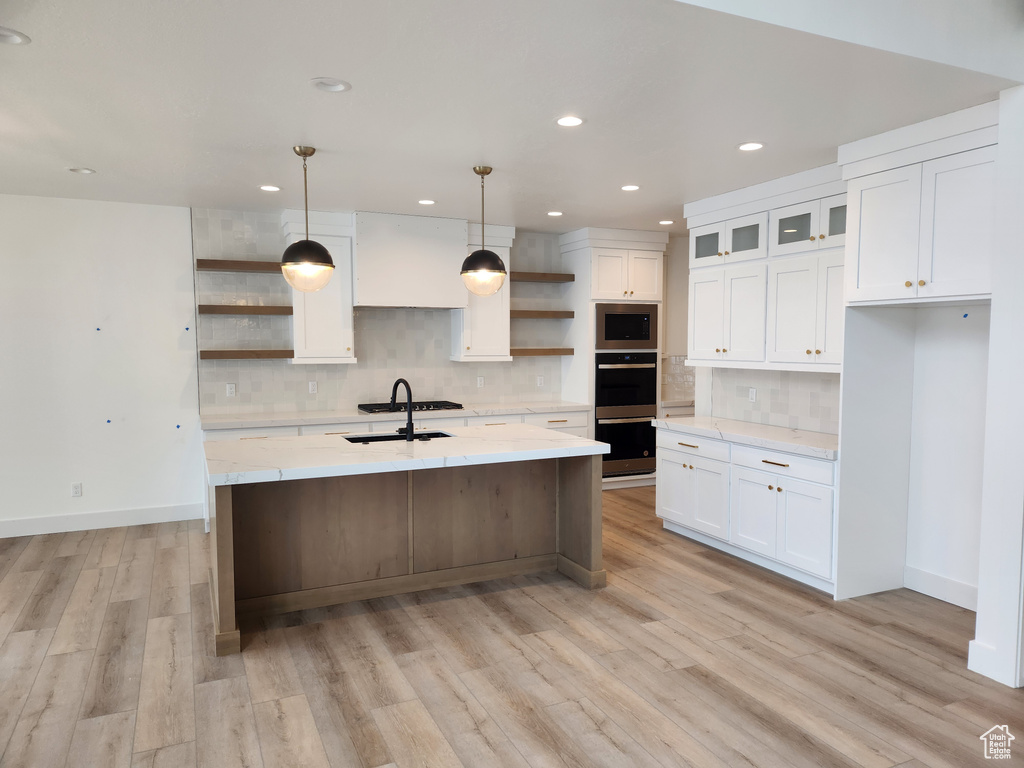 Kitchen featuring light hardwood / wood-style flooring, tasteful backsplash, white cabinetry, and a kitchen island with sink