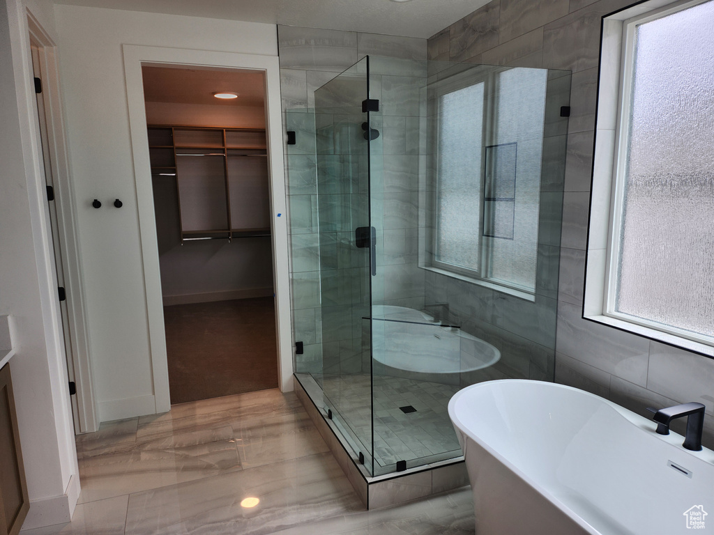 Bathroom featuring plenty of natural light, separate shower and tub, tile flooring, and tile walls