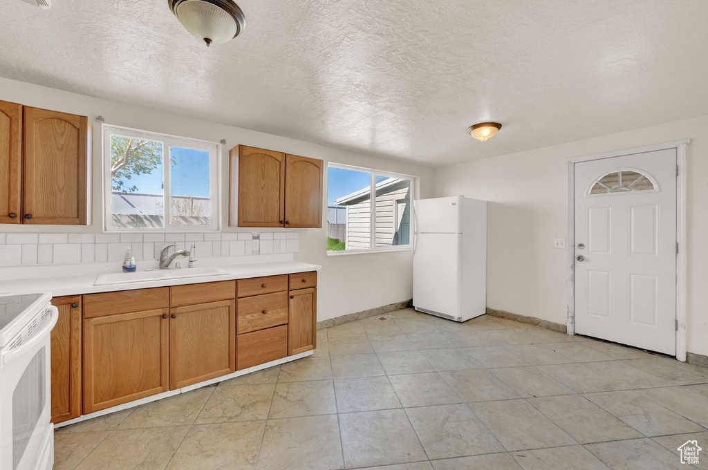 Kitchen featuring light tile flooring, range, white refrigerator, sink, and tasteful backsplash