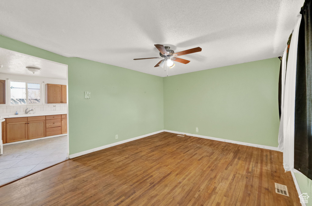 Unfurnished room with sink, ceiling fan, a textured ceiling, and light wood-type flooring