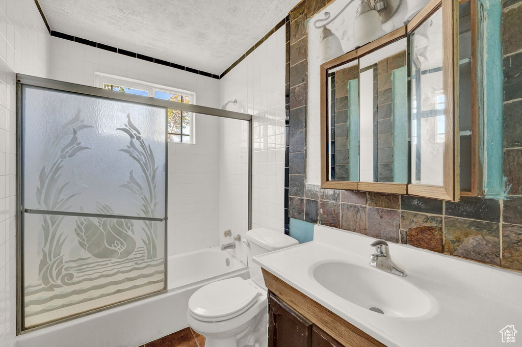Full bathroom featuring tile walls, a textured ceiling, combined bath / shower with glass door, toilet, and vanity