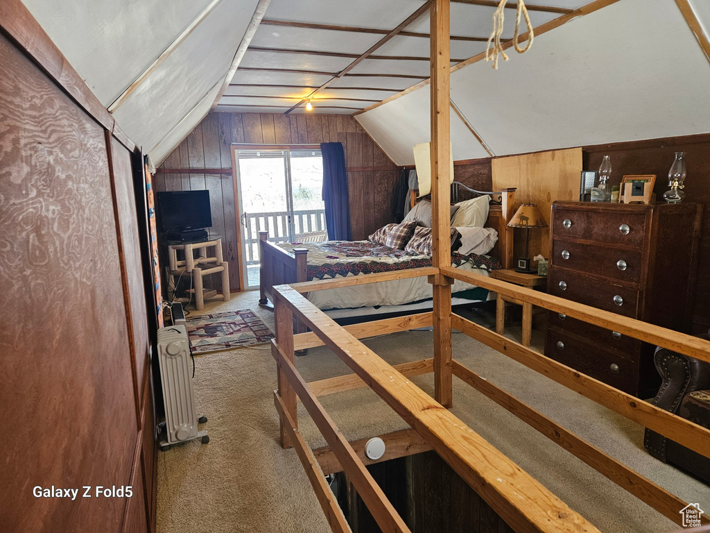 Bedroom with lofted ceiling, radiator, carpet flooring, and wooden walls