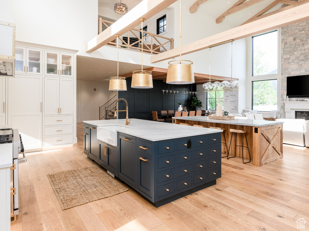 Kitchen with a fireplace, light wood-type flooring, white cabinetry, a high ceiling, and an island with sink