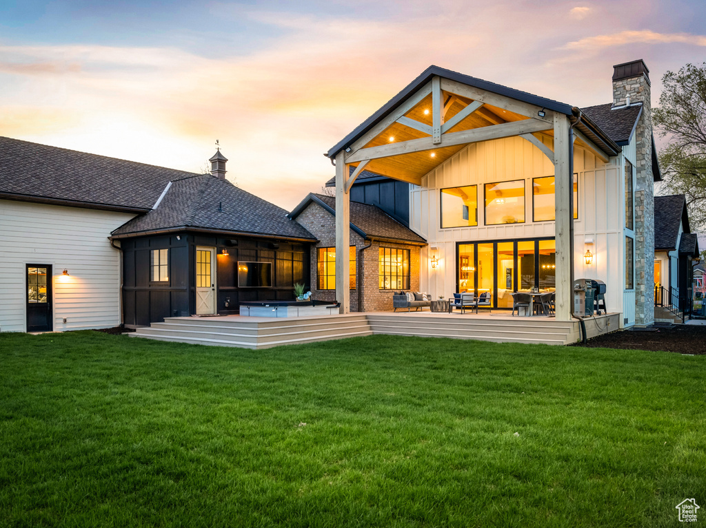 Back house at dusk with a patio area, a sunroom, and a lawn