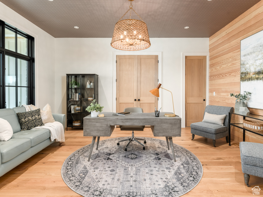 Home office with wooden walls, an inviting chandelier, and light wood-type flooring