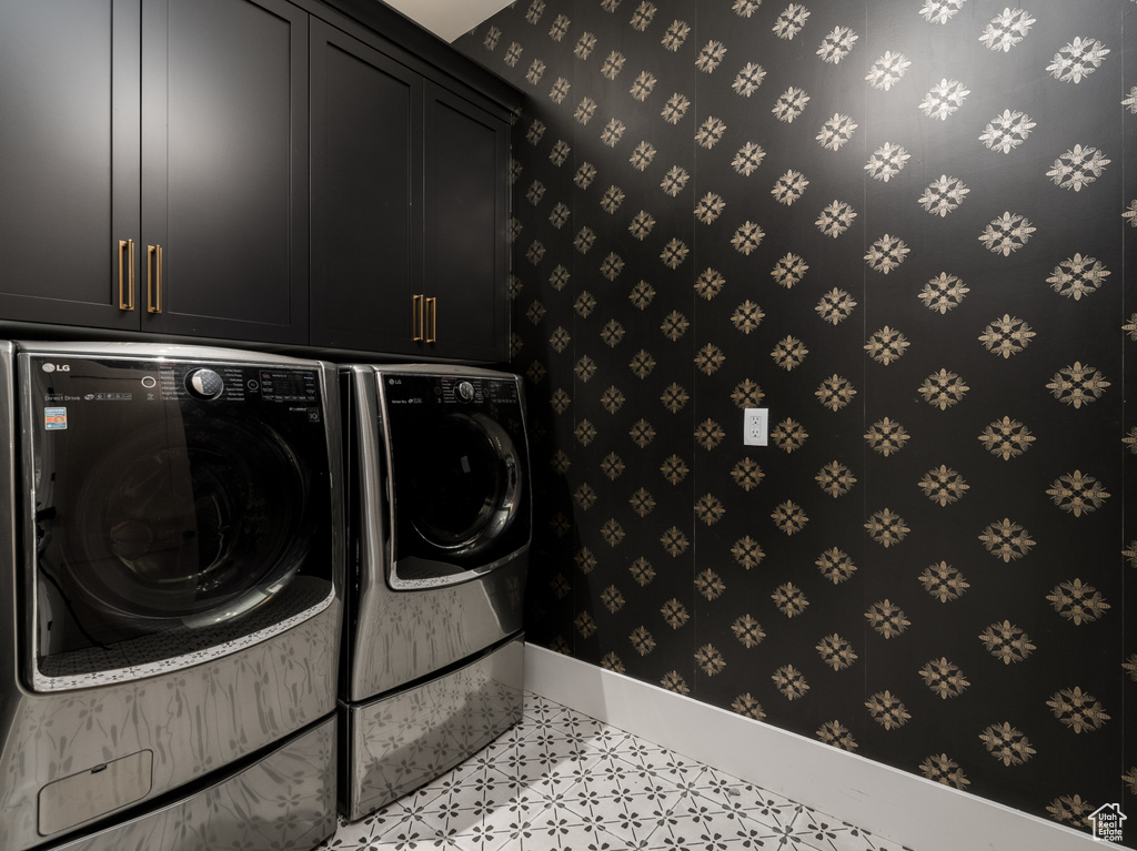 Clothes washing area featuring washing machine and dryer, cabinets, and light tile floors
